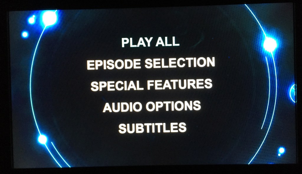 Doctor Who DVD Audio Menu Screen - Main Menu, showing Play All, Episode Selection, Special Features, Audio Options and Subtitles, all in large clear print. Background behind text is black - circular shapes and lights adorn the edges.