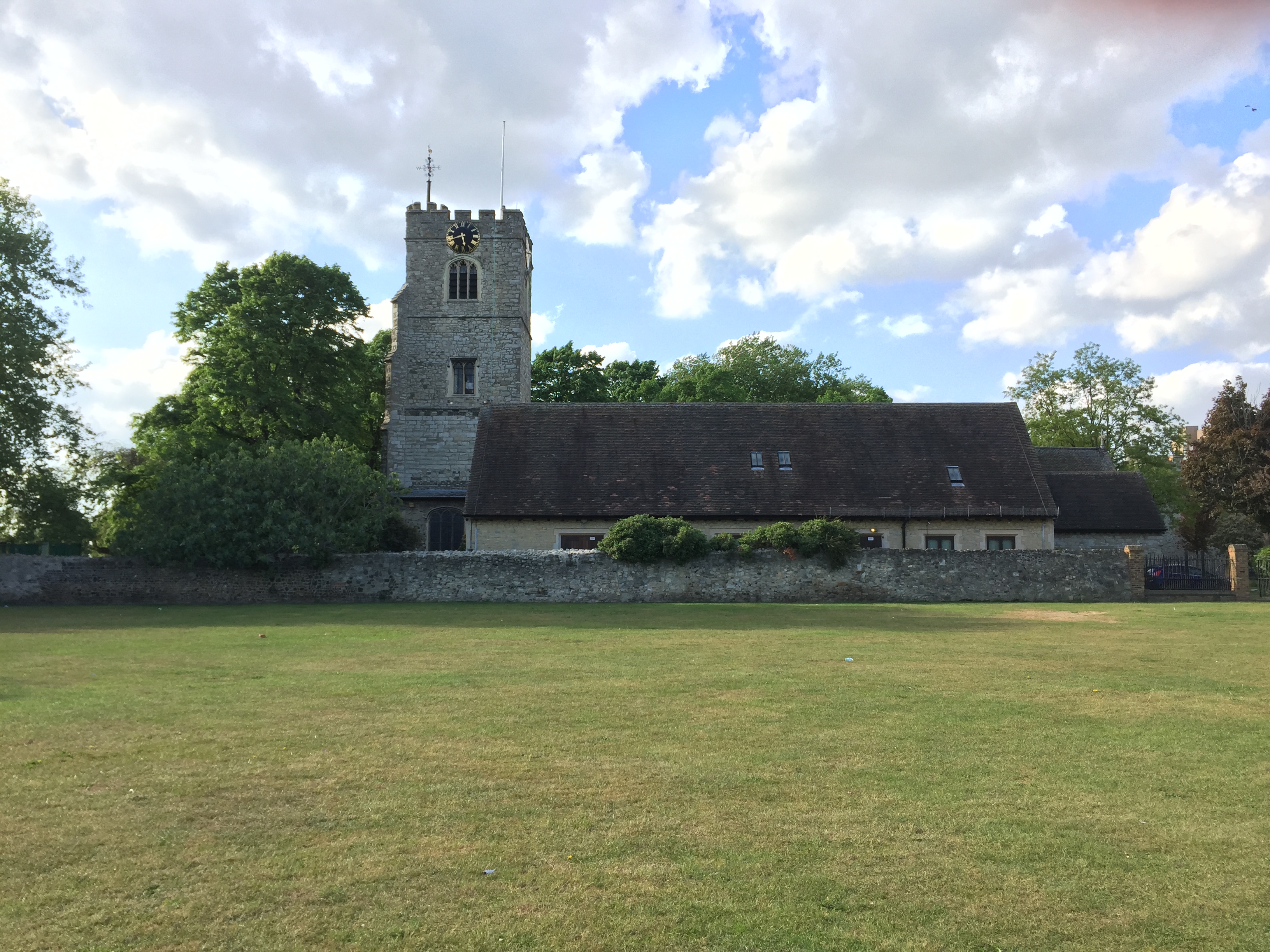 A large area of grass in front of a long bungalow and a tall stone tower in the grounds of Barking Abbey.