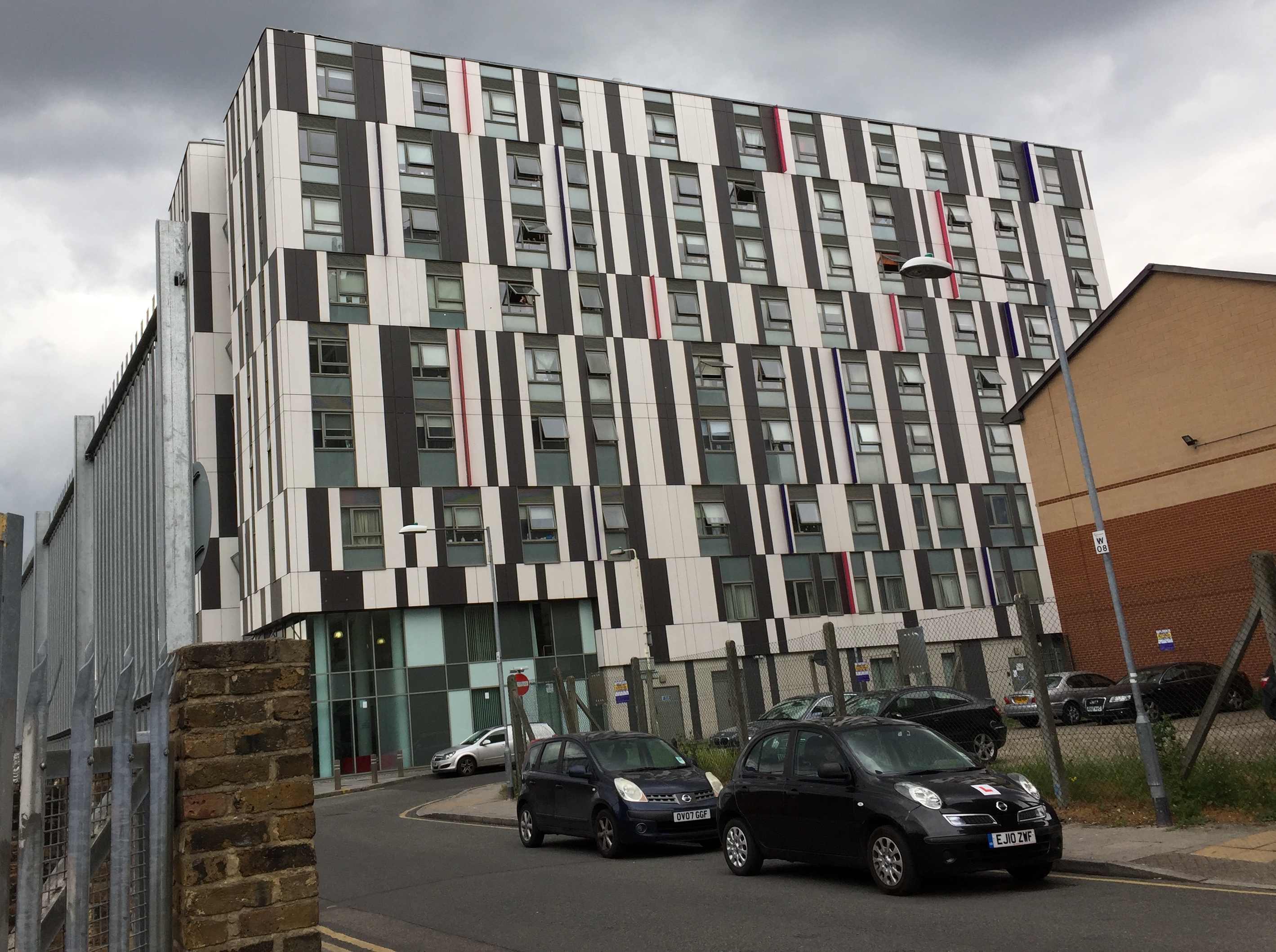 The Barking Enterprise Centre BEC 2 building. The building appears to have 8 floors. However, of the 7 floors above ground level, the top, middle and bottom floors have their windows shifted slightly to the right compared to the other floors, giving the building an uneven appearance. The walls along each floor also have alternating black and white vertical stripes of varying width, and the window frames are also black, so each floor looks a bit like a barcode with windows in it.