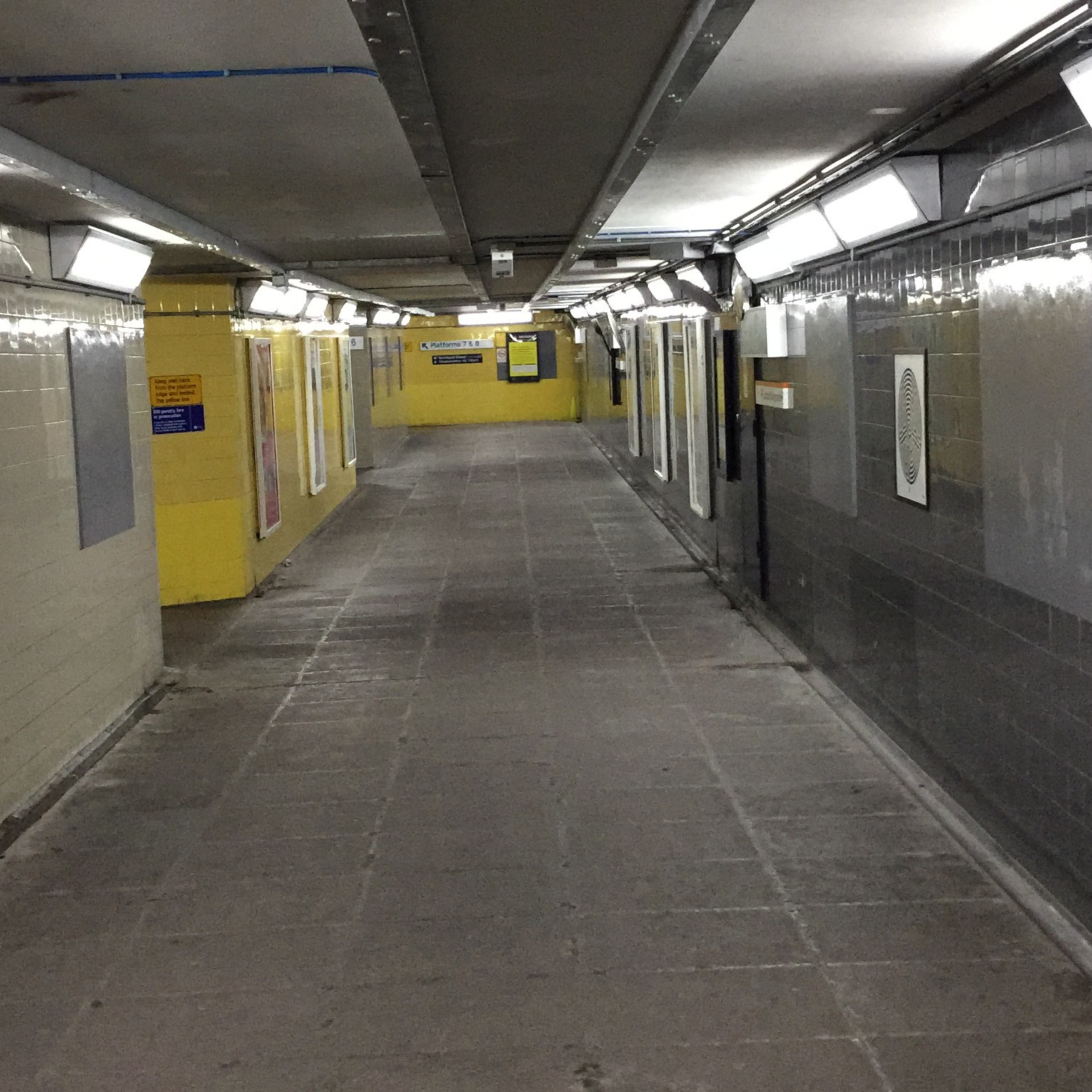Pedestrian subway linking the platforms at Barking Station. The walls along the left and at the far end are yellow, while the wall along the right side is dark grey.
