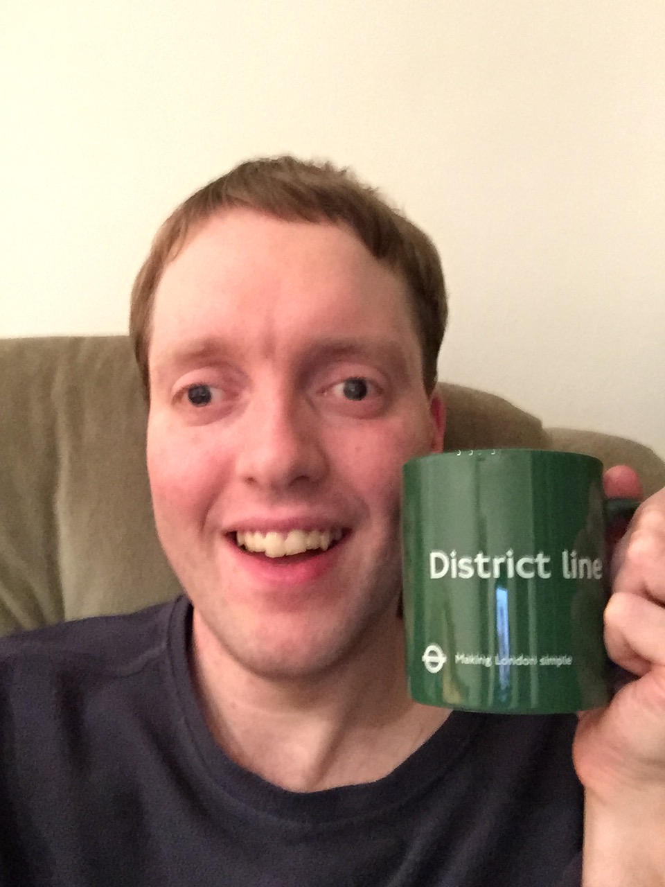 Me holding a green mug, which has District Line in big white letters in the centre. Below that, in smaller white print, is the London Transport roundel logo, with the words Making London Simple.