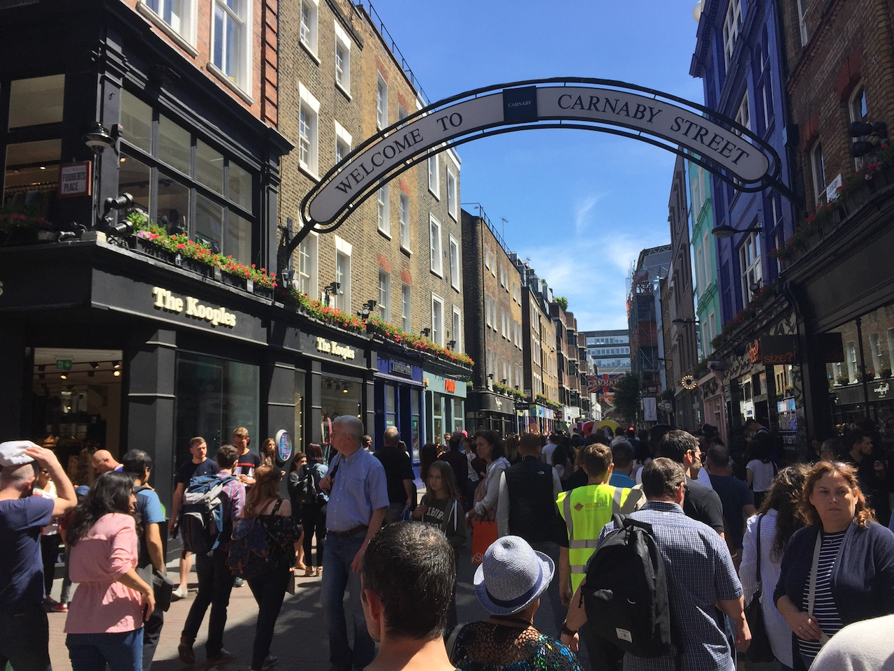 An arched sign that says Welcome To Carnaby Street, with a big crowd of people walking beneath it.