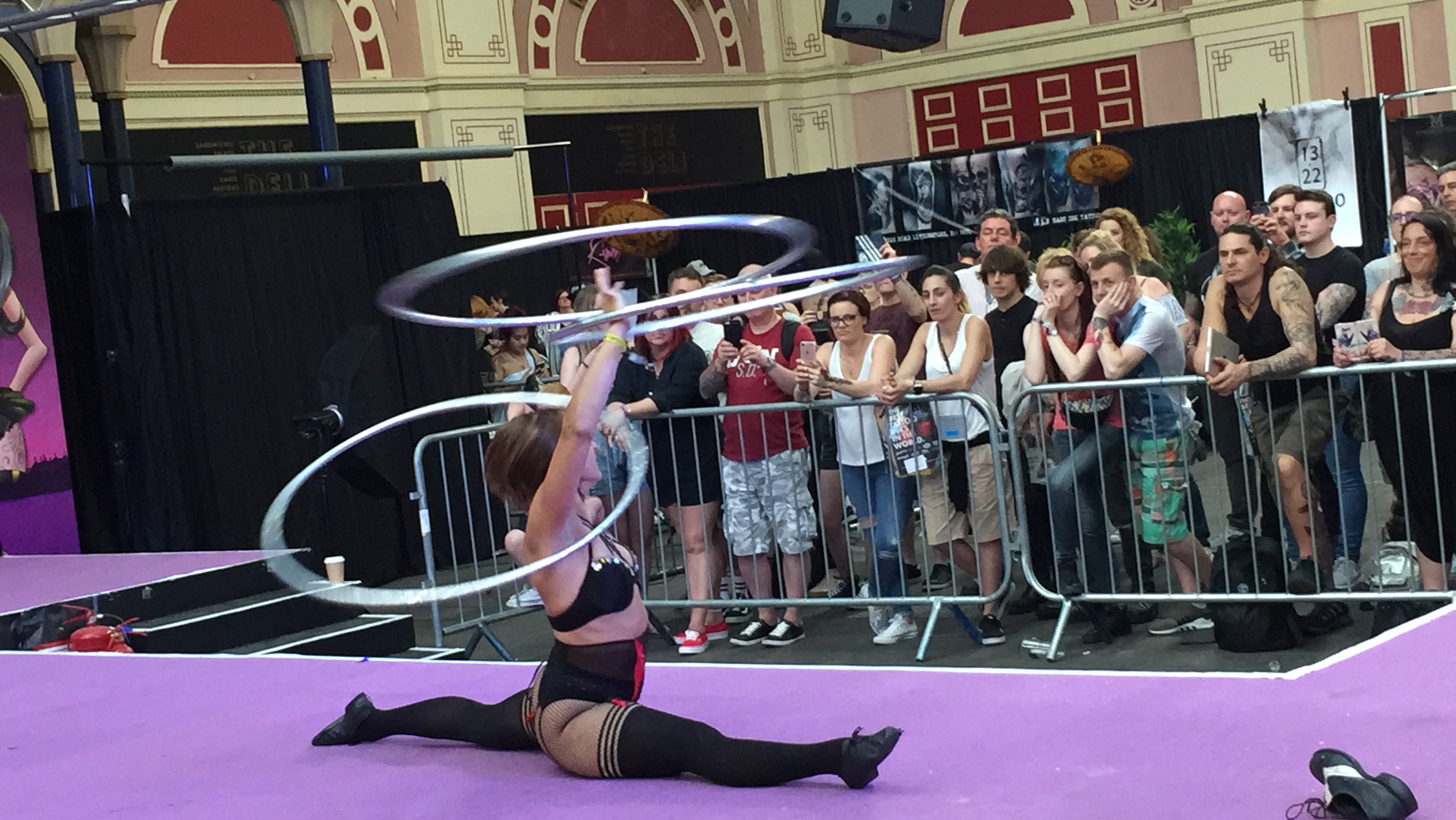 Lady doing the splits while hula-hooping with 3 large hoops
