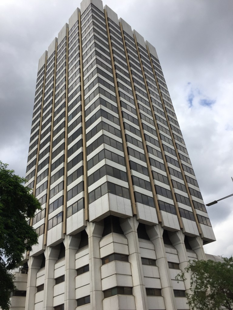 The ITV Studios tower. Above a ground floor that is large enough to accommodate the studios, there are 19 rows of narrow windows across 5 columns, on each side of the building. Each row is separated by white brickwork, and each column is separated by a indented gap, filled with a narrow brown column from the roof down to the larger white brick columns on the ground floor.