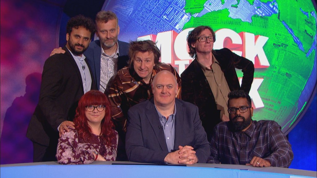 Group photo showing the guests gathered around Dara O Briain, in front of a large image of the Earth with Mock The Week in large text on top. On Dara's left is Angela Barnes, to his right is Romesh Ranganathan. Behind them, from left to right, are Nish Kumar, Hugh Dennis, Milton Jones and Ed Byrne.