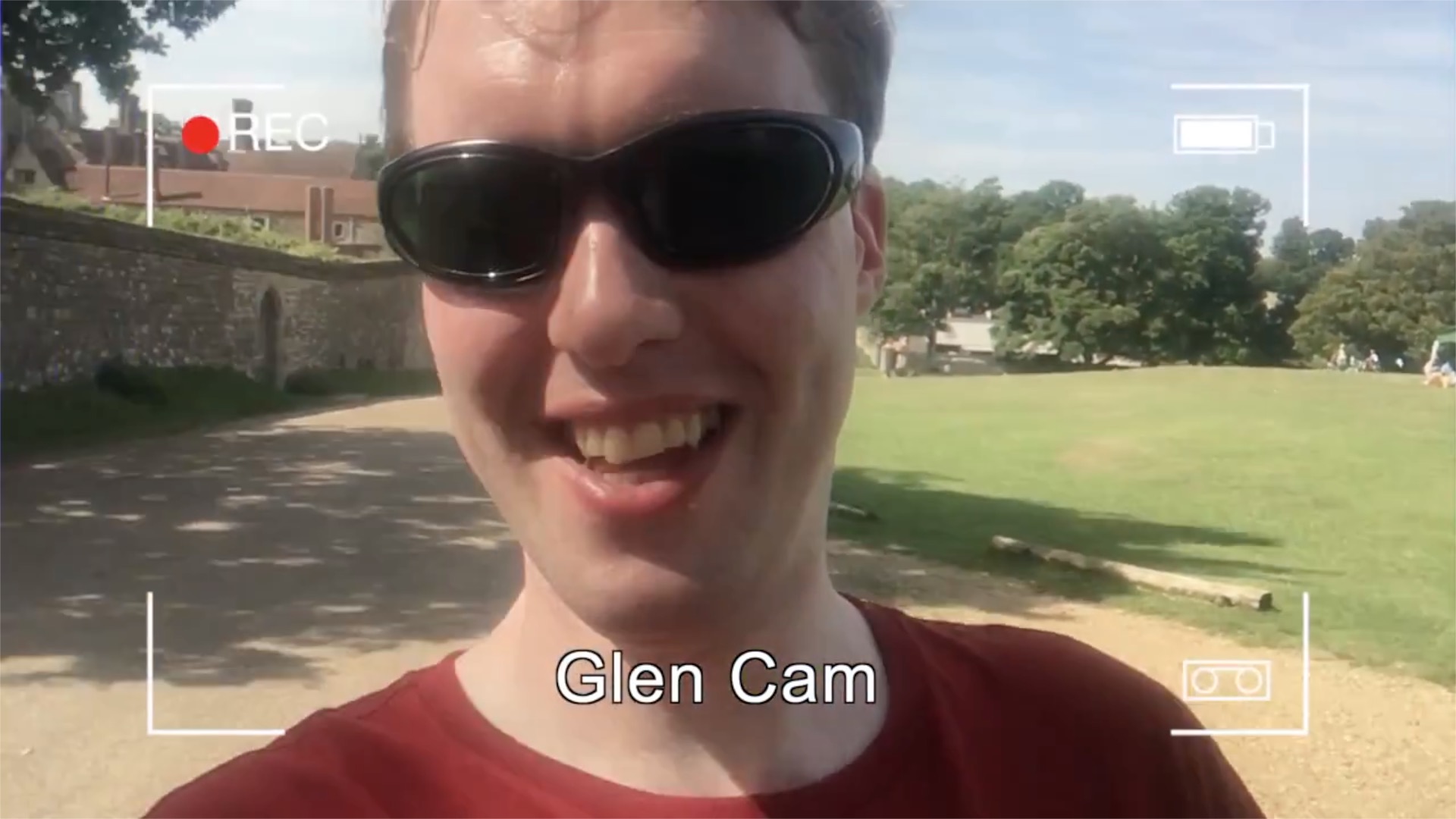 Glen wearing sunglasses and smiling at the camera in the sunshine. Overlaid on the image is a mockup of a camera recording screen, with 4 right-angled corner marks, a recording symbol top-left, a battery level indicator top-right, and the words Glen Cam centred at the bottom.