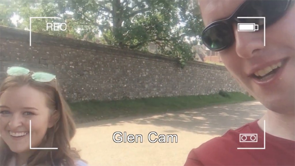Emily and Glen smiling at the camera in the sunshine. Overlaid on the image is a mockup of a camera recording screen, with 4 right-angled corner marks, a recording symbol top-left, a battery level indicator top-right, and the words Glen Cam centred at the bottom.