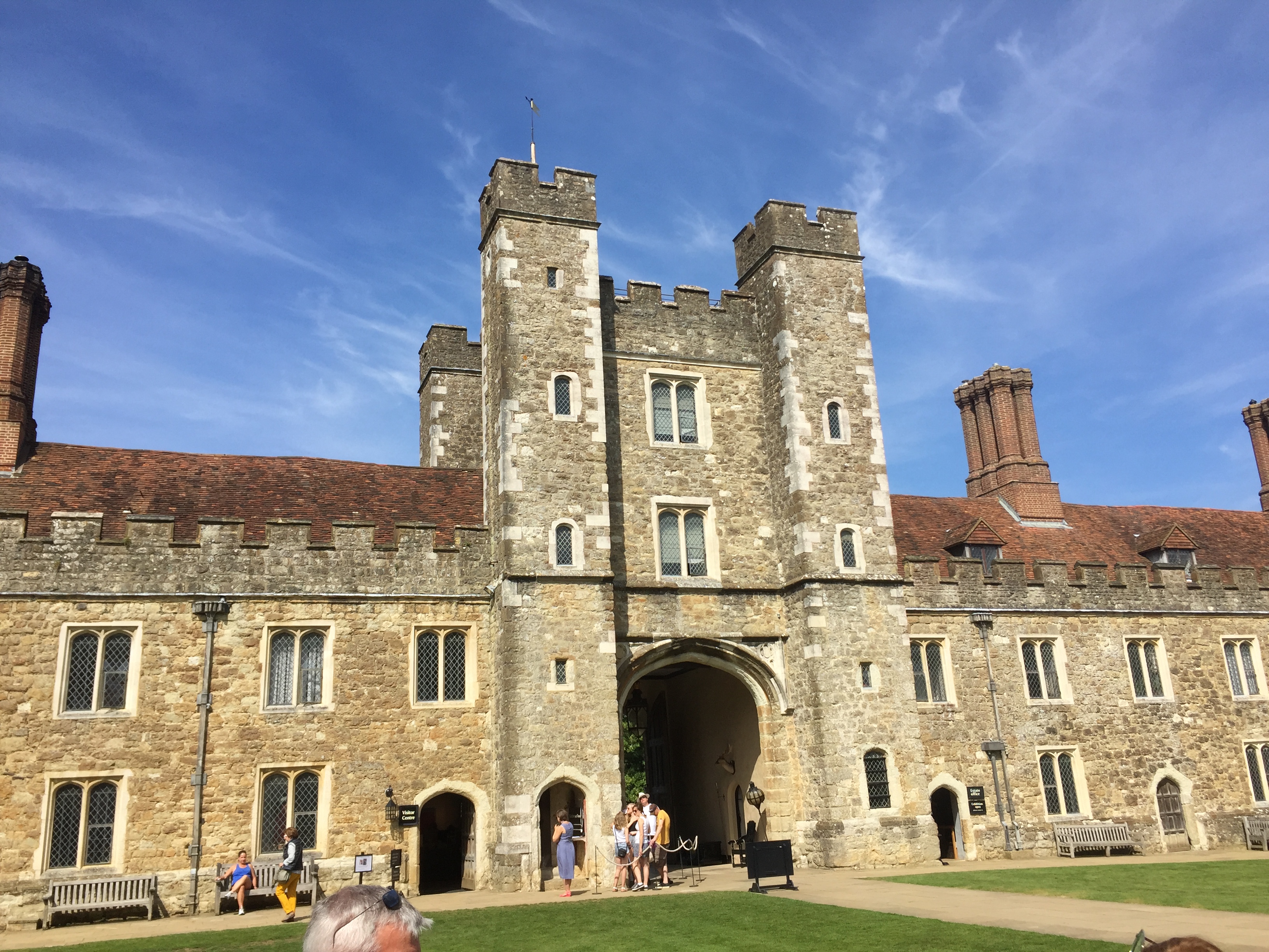 Knole House, a large stone building. In the centre are 2 towers with 5 floors, in between which is a wider tower with a large archway and 2 floors above it. Extending to each side, the lengthy extensions of the building are only 2 storeys high, with chimneys on top.
