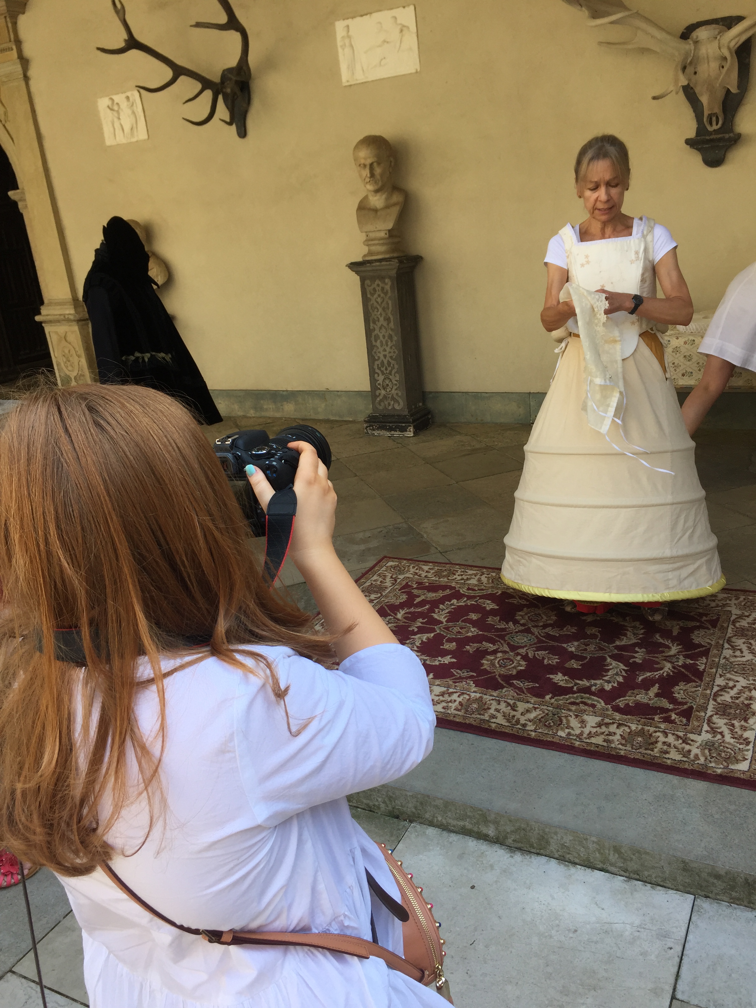 Emily taking a photo of a lady dressing up in the various layers of a Tudor outfit.