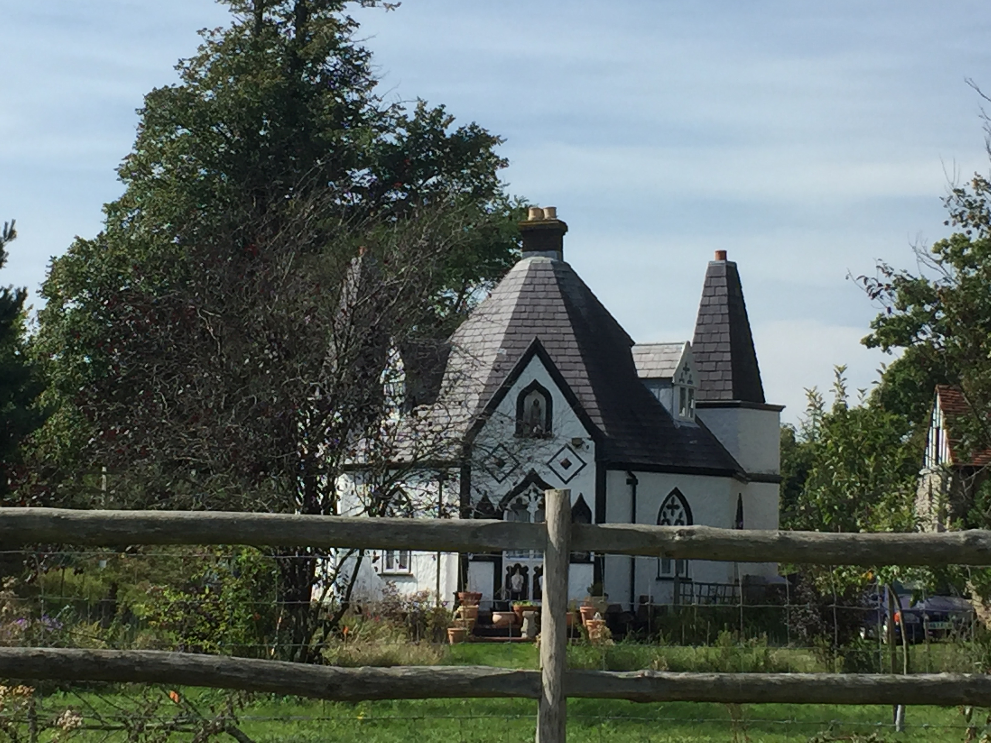 A white building, with a pointed roof made of brick, and with tall windows and front door that all curve to a point at the top. 2 black-edged diamond shapes sit just above the front door, with a smaller black diamond in the centre of each.