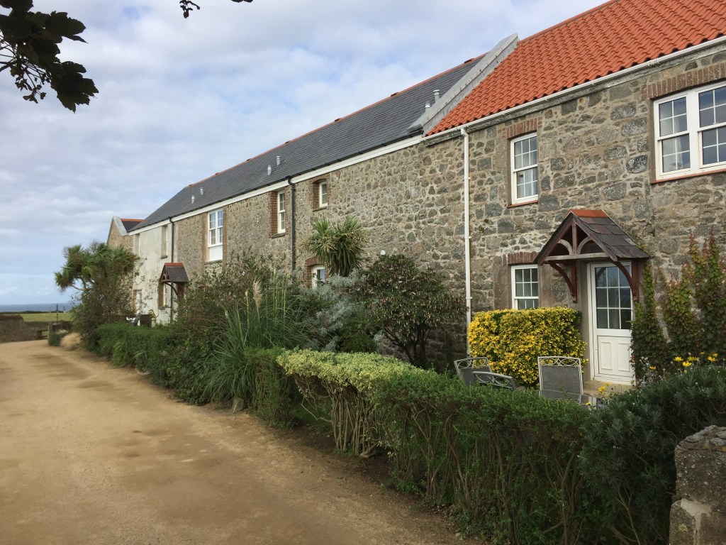 A row of terraced stone houses on Herm island, with small canopies over the doors and low hedges around the gardens.