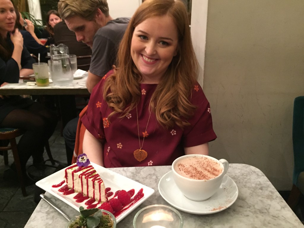 Emily with a slice of lime cheesecake covered in raspberry sauce, and a large mug of hot chocolate.