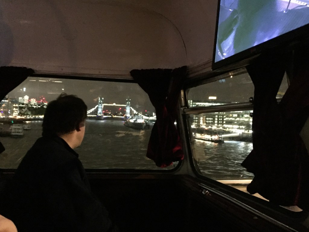 View of Tower Bridge in the distance, lit up in the night sky. Viewed from the top deck of the bus as we cross London Bridge.