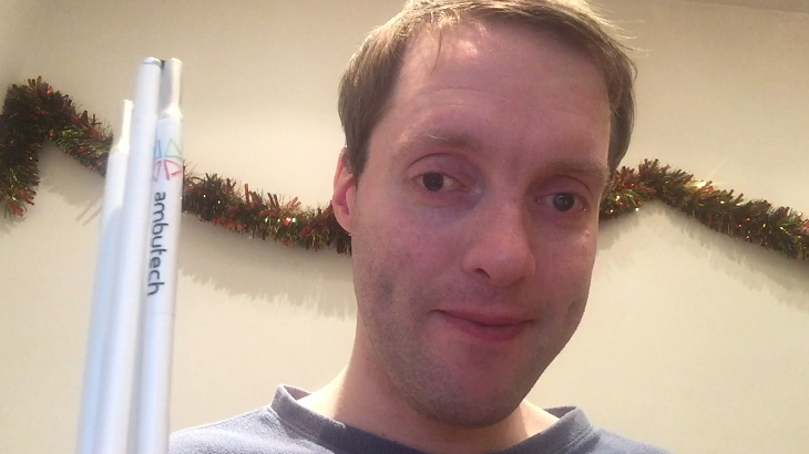 Me holding a folded up white symbol cane, with tinsel along the wall in the background.