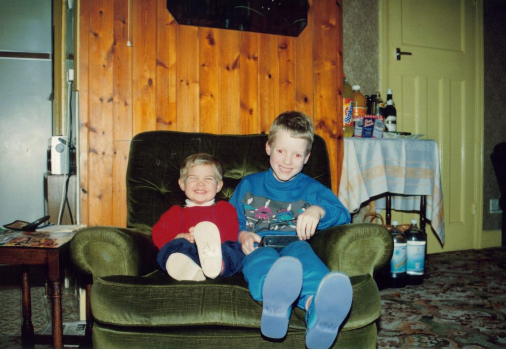 Me as a young child, with my cousin of a similar age, sitting together on a big wide armchair and smiling.