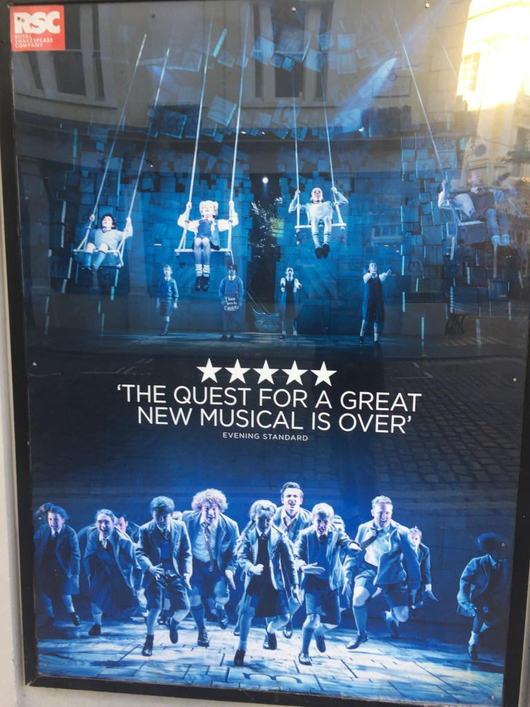 Tall poster with 2 photos - children on swings at the top, and children dancing on the bottom. In between is a quote from an Evening Standard 5-star review, saying the quest for a great new musical is over.