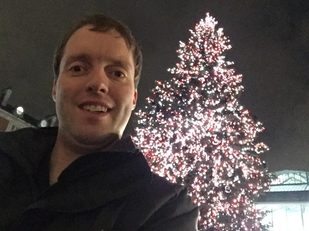 A selfie of me standing in front of the massive Covent Garden Christmas tree, which is covered in bright lights.