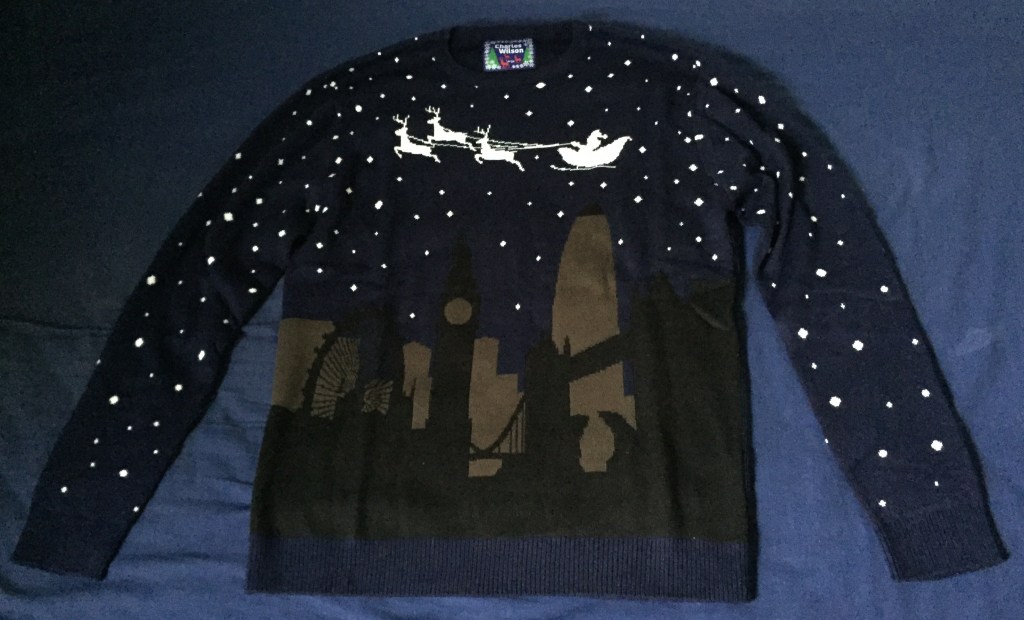 Navy jumper with black and brown silhouettes of London landmarks on the bottom half, while white silhouettes of Santa and 3 reindeer fly over the top. White stars cover the background of the entire jumper.