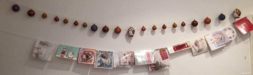 Baubles threaded along a line of string across the wall, above a line of Christmas cards hanging over another length string along the wall.