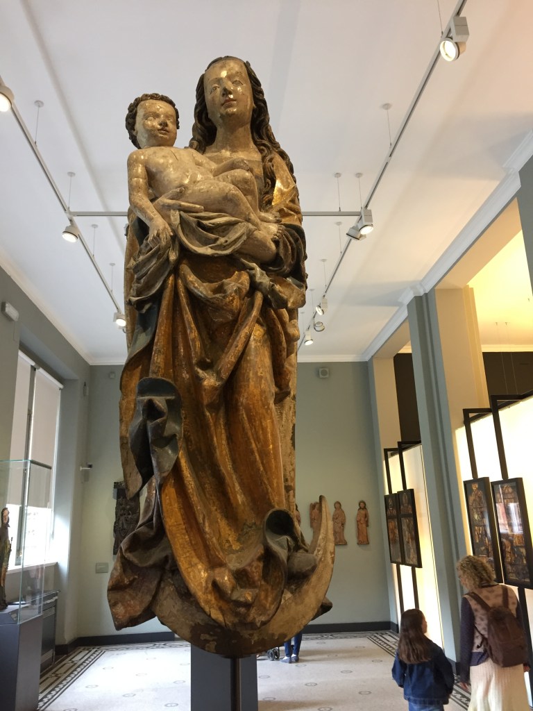 Tall bronze statue of a mother in long robes holding a baby.