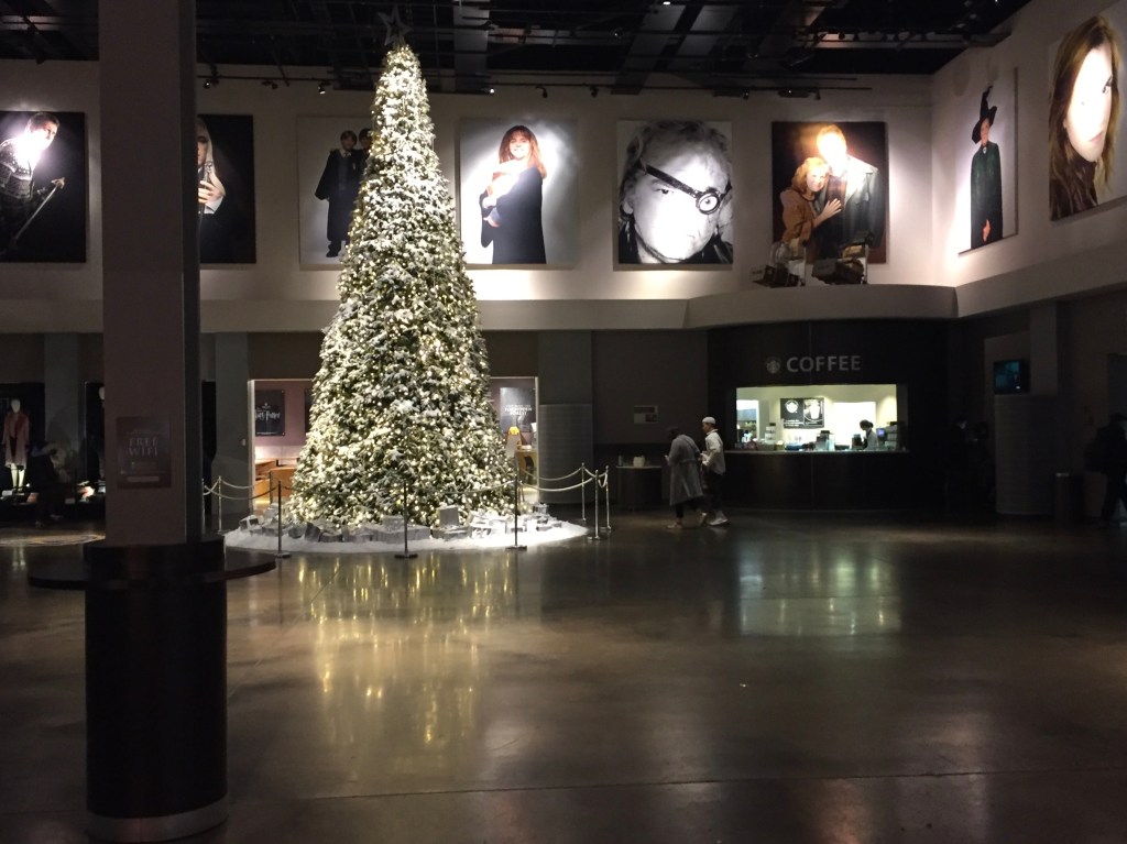 Very tall Christmas tree covered in lights in the large studio reception area, with large photos of various characters from the Harry Potter movies all around the upper walls