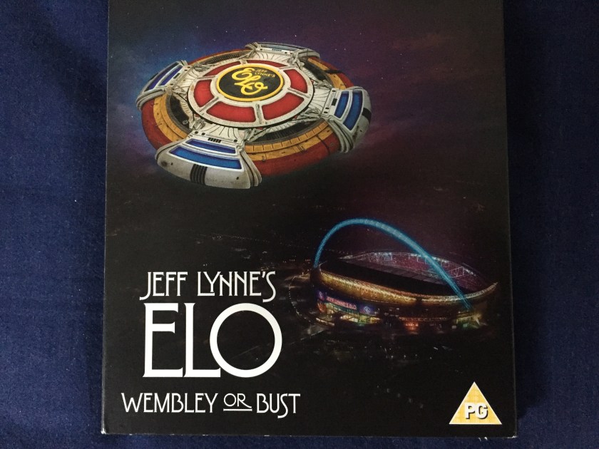 Square black CD case for Jeff Lynne's ELO - Wembley Or Bust, showing a picture of Wembley stadium with what appears to be a large round spaceship with the ELO logo flying over it.