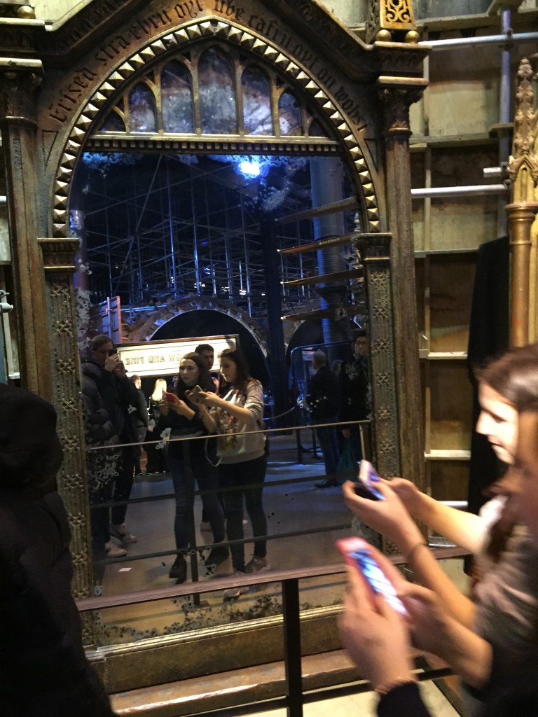 Two girls taking photos on their phones in front of the tall and ornate Mirror Of Erised.