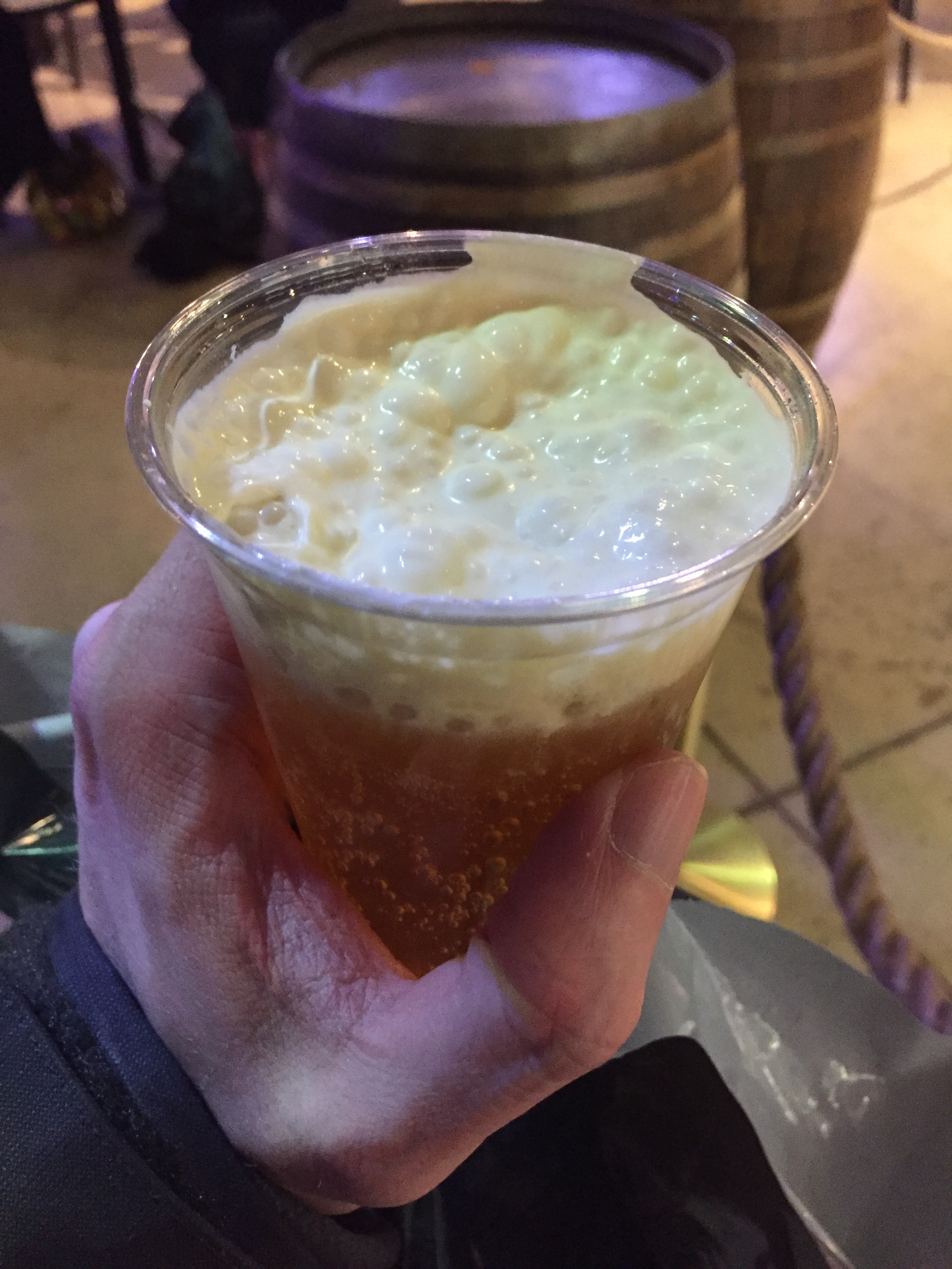 A plastic glass filled with Butterbeer, with a foamy head.