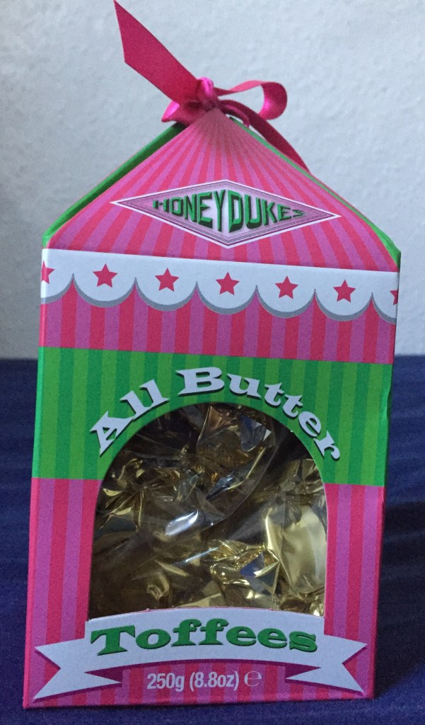 Pink and white box for Honeydukes All Butter Toffees, with the sweets visible in gold wrappers through the plastic window.