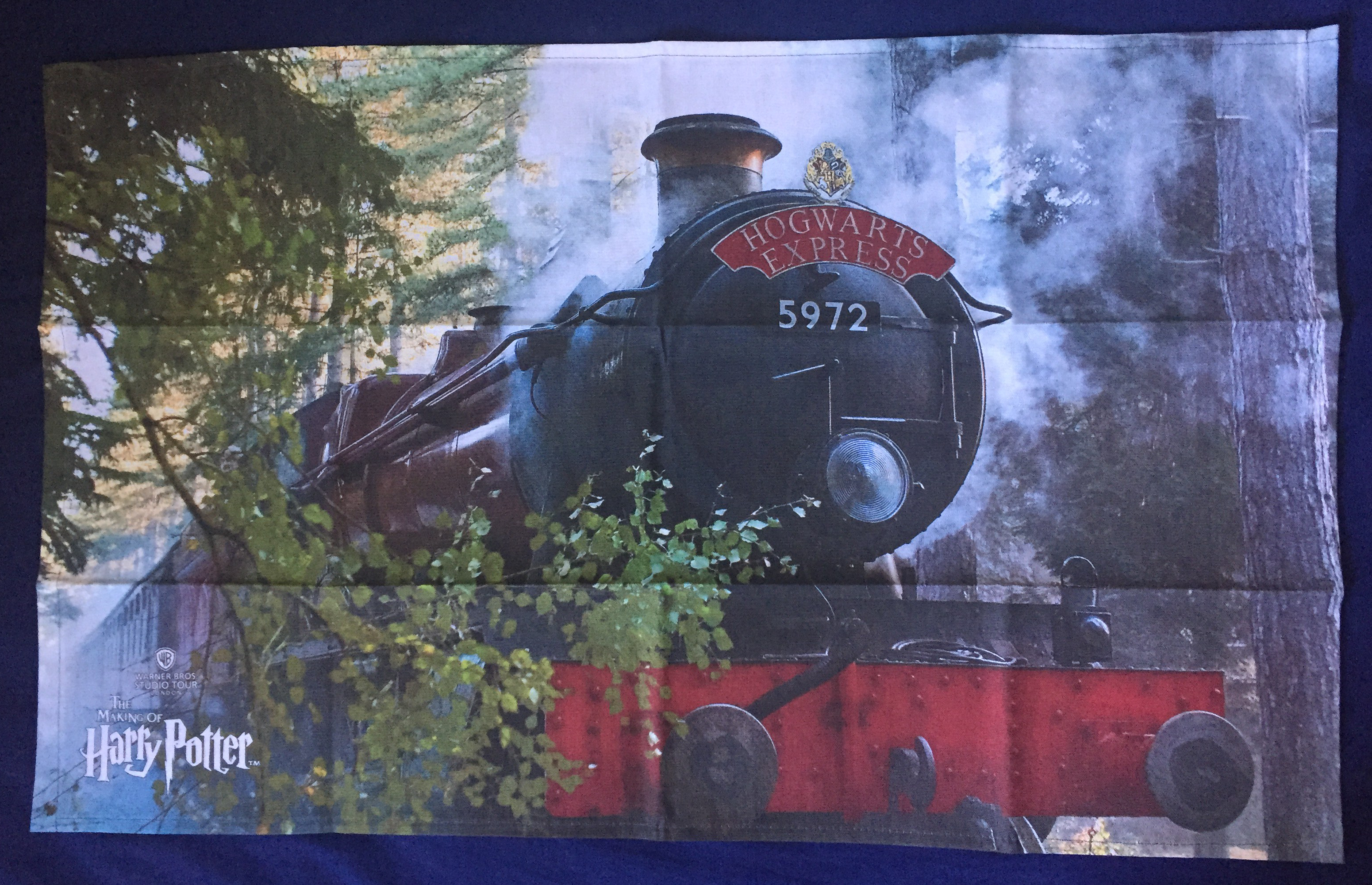 Tea towel showing a large image of the Hogwarts Express steam train passing by trees that line the edge of the railway.