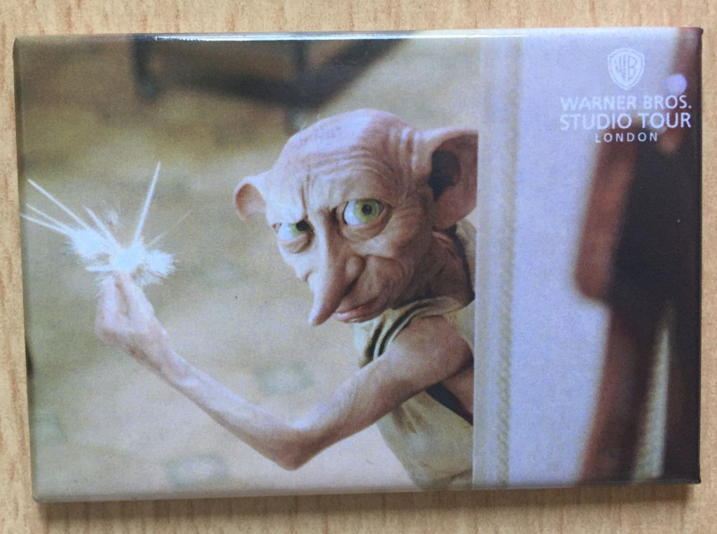 Fridge magnet showing Dobby the House Elf peering around a doorway and looking at us, producing sparks as he clicks his fingers.