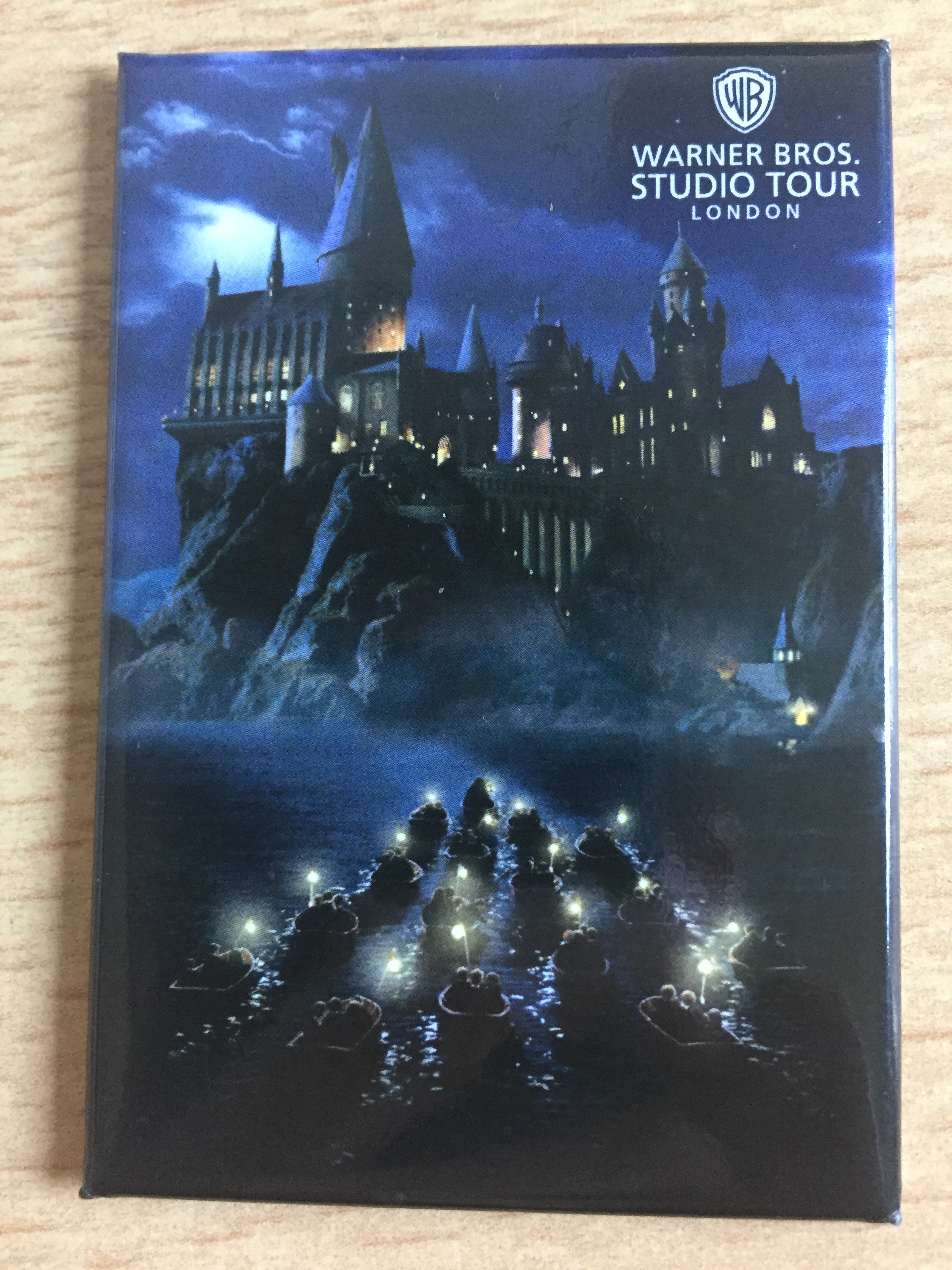 Photo magnet showing a night time scene, with people in small boats holding lights as they travel across the water, heading for the enormous Hogwarts Castle ahead of them.