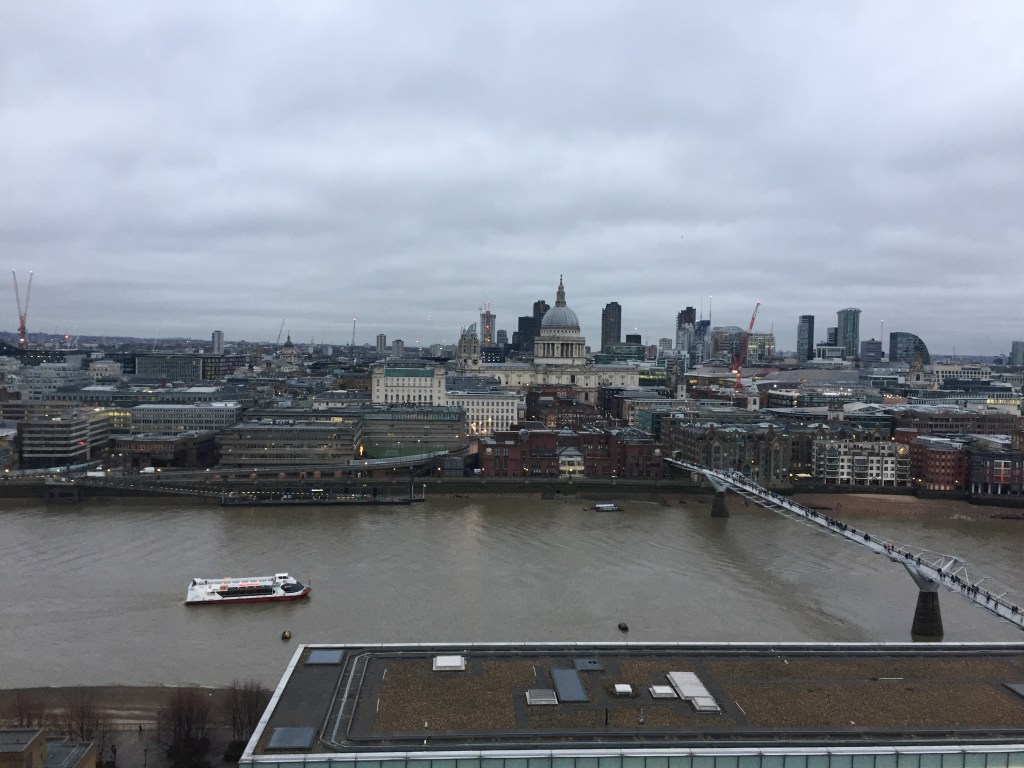 View across the Thames, high up on level 10 of the Tate Modern. St Paul's Cathedral is directly opposite, while on the river a tourist boat is travelling towards the Millennium Bridge on the right.