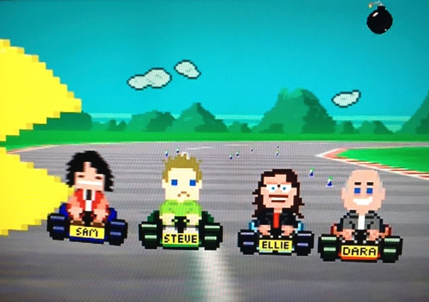 Image from the Go 8 Bit title sequence shows blocky computer graphic versions of Dara and his 3 main co-stars driving around a race track in small cars, while a large Pac-Man figure enters from the left.