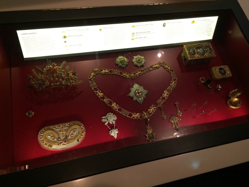 Glass case containing various jewellery items, including a large ornate necklace in the centre.