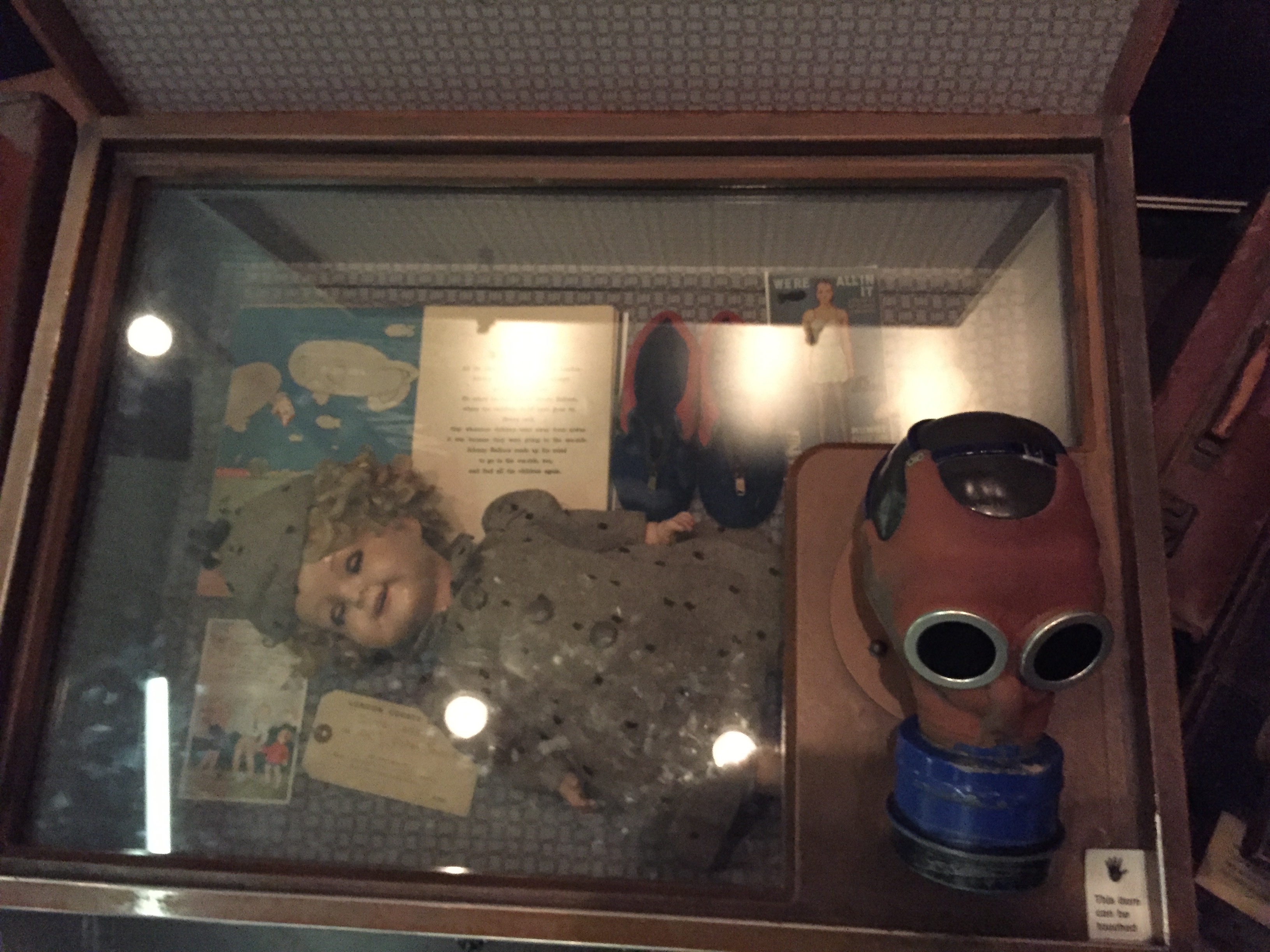 A case used for transporting a child's possessions during evacuation. This one contains a doll and books, and on to of the case is a child's gas mask, which you can touch.