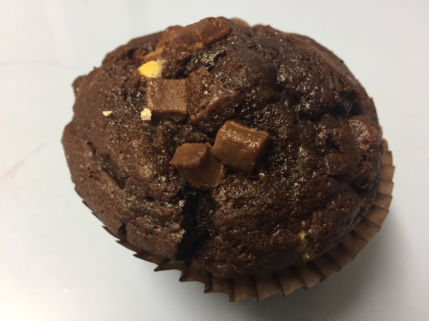 A large round chocolate muffin, decorated with chunks of chocolate.