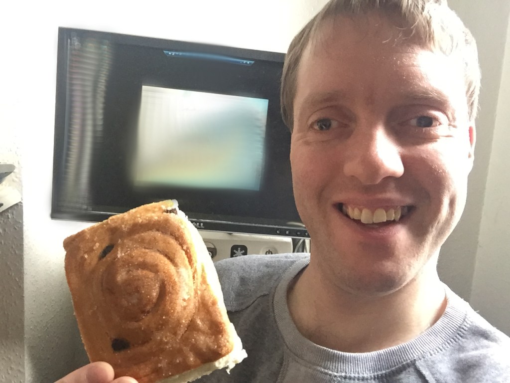 Me sitting in front of my computer screen, smiling and holding a square cake with a swirly design on top.