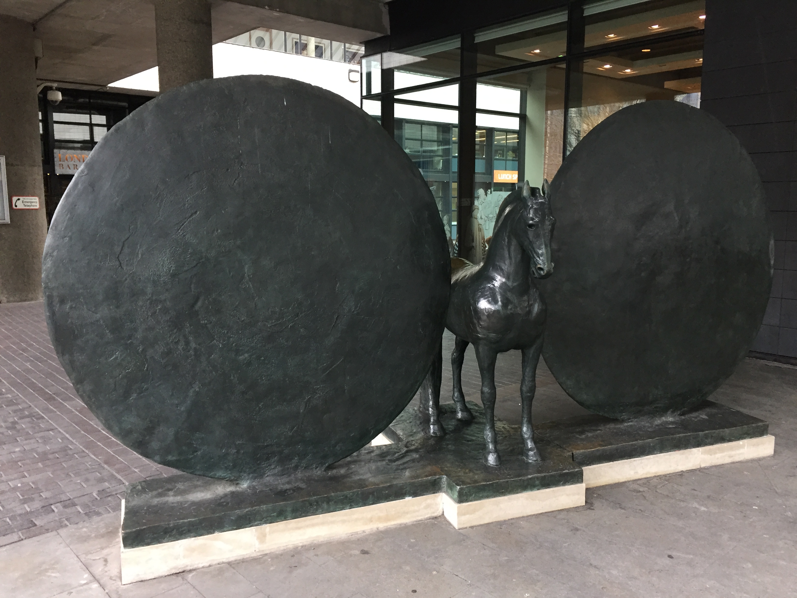Sculpture of a black horse between 2 large black round shields, by the entrance to the museum.