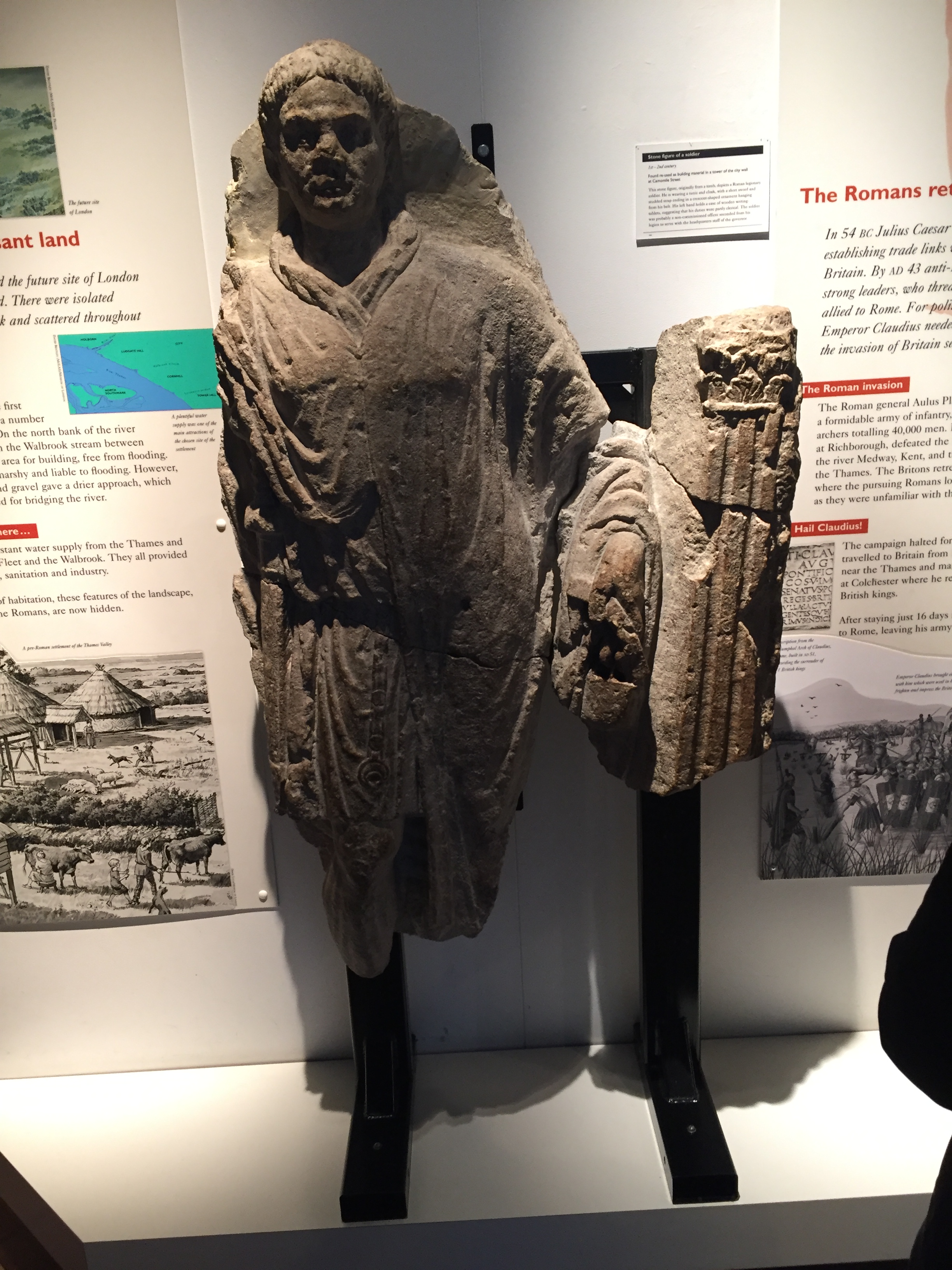 Large rocky statue of a Roman man, in front of white panels on the wall containing text and images about the era.