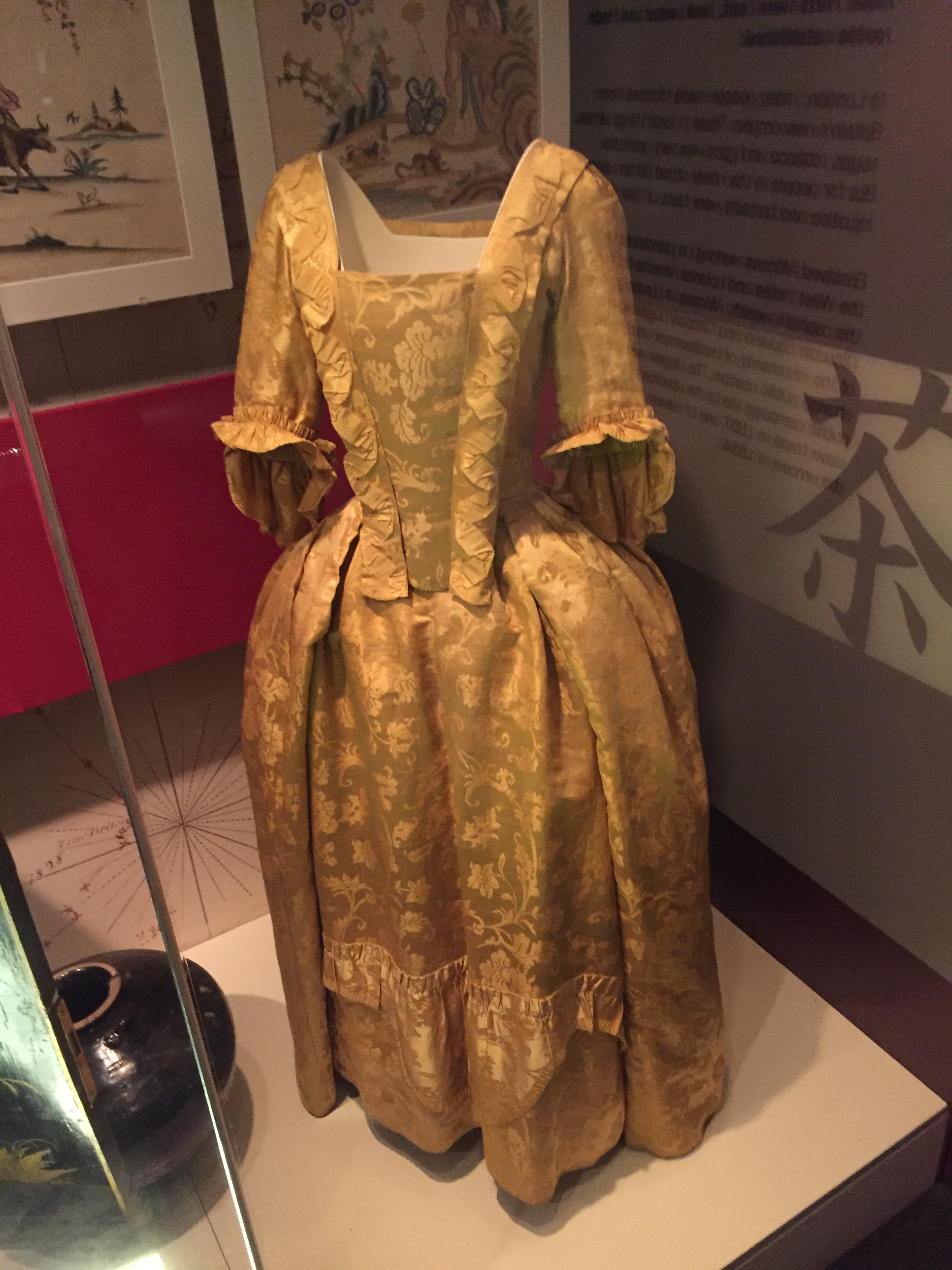 A long, full golden dress with flowery patterning and ruffled edging.