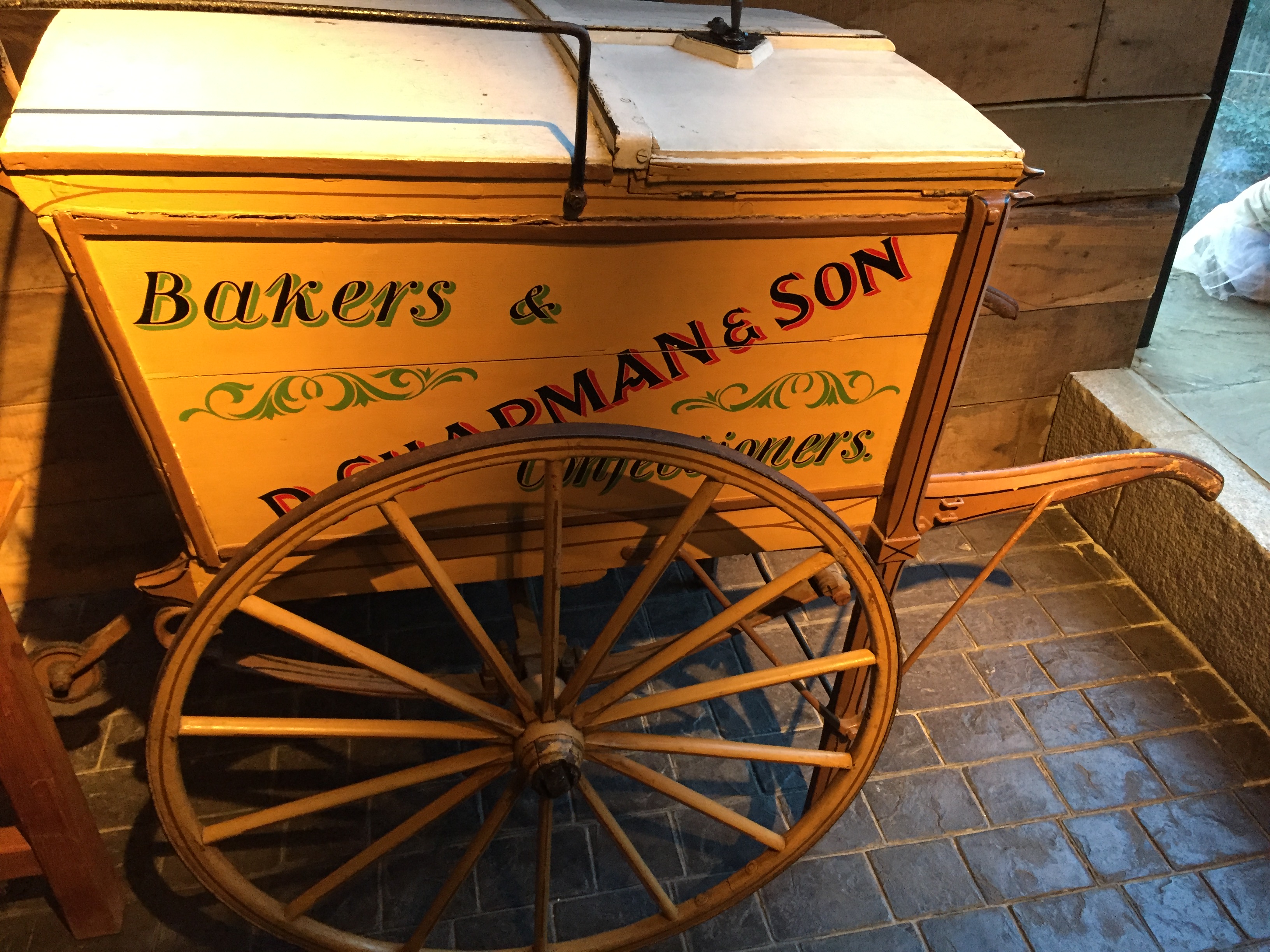 A yellow Victorian bakers and confectioners wagon, with 1 large wheel on each side.