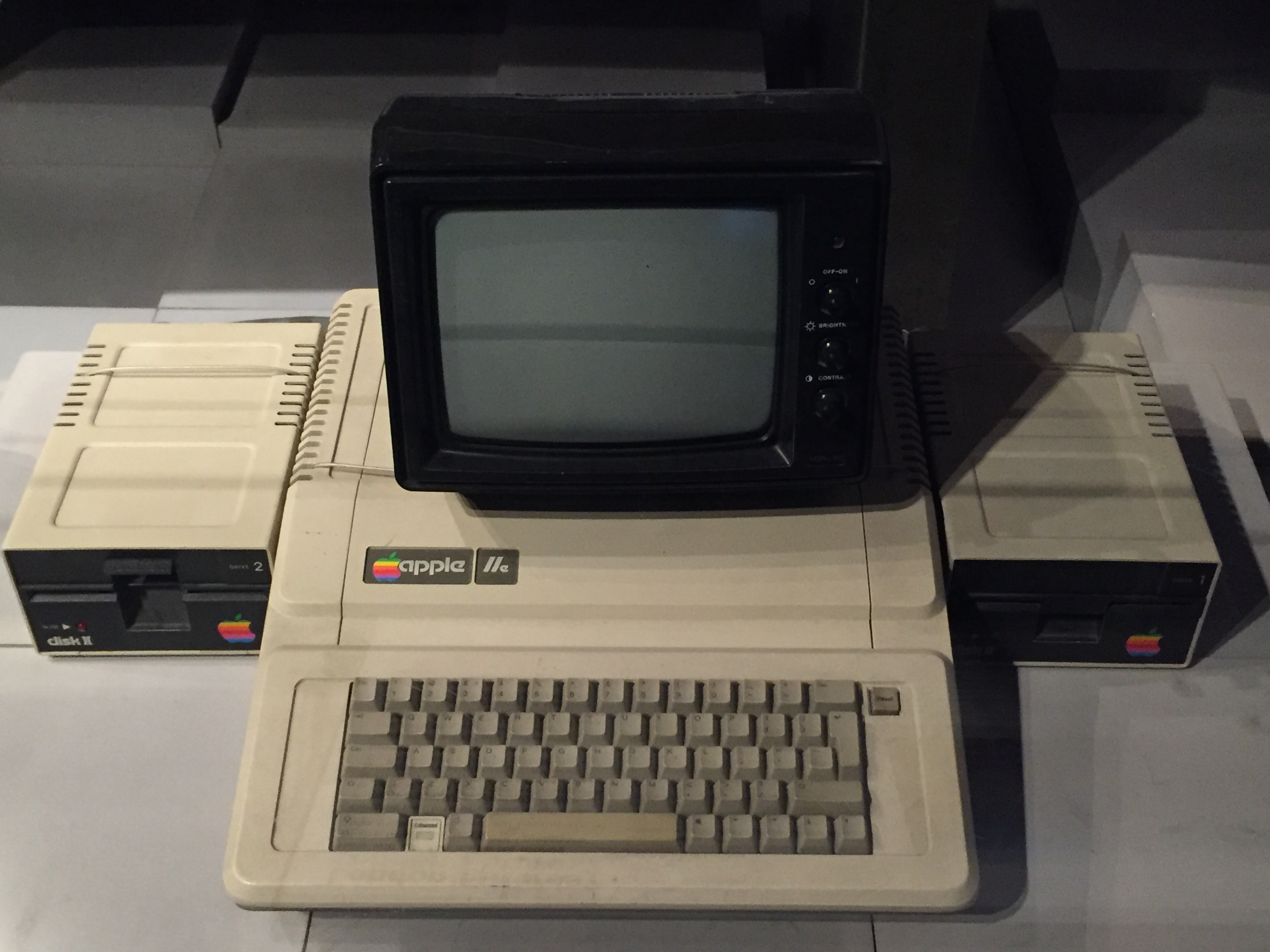 An Apple 2E computer, with a keyboard, small bulky monitor and drives for floppy disks.