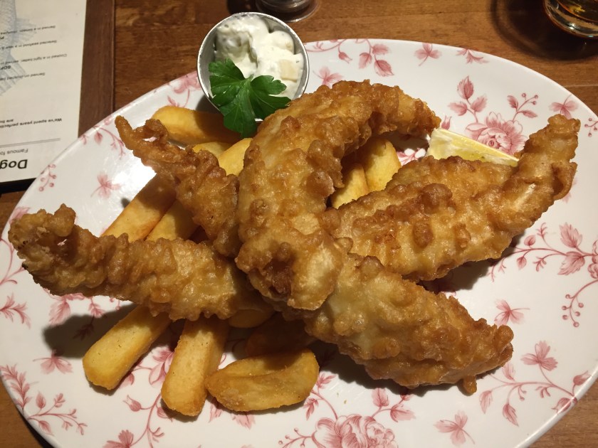 3 long pieces of battered cod on top of chunky chips, with a small pot of tartare sauce.