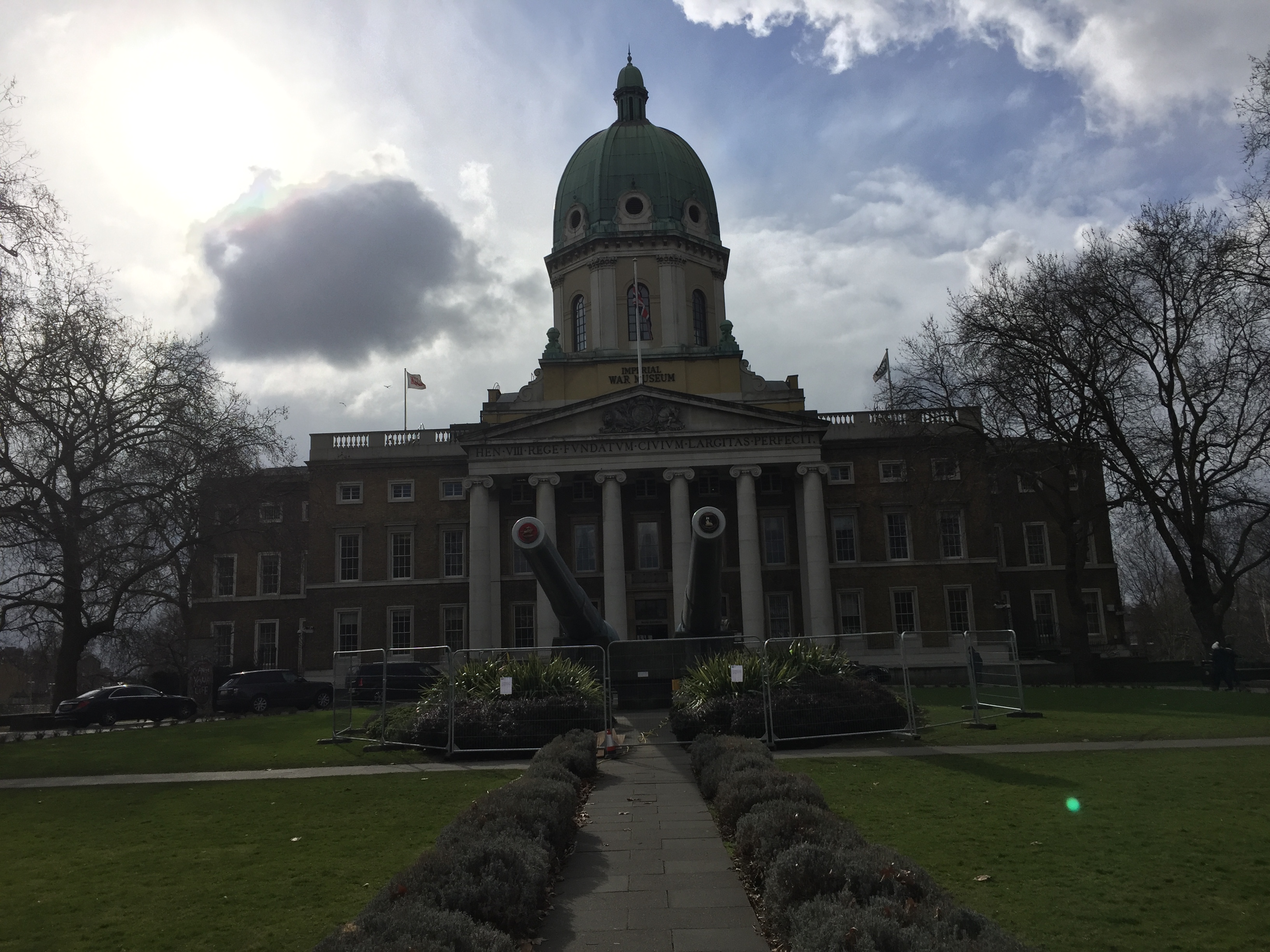 Exterior of the Imperial War Museum building, with 2 large cannons pointing towards the camera from the centre of the circular garden area.