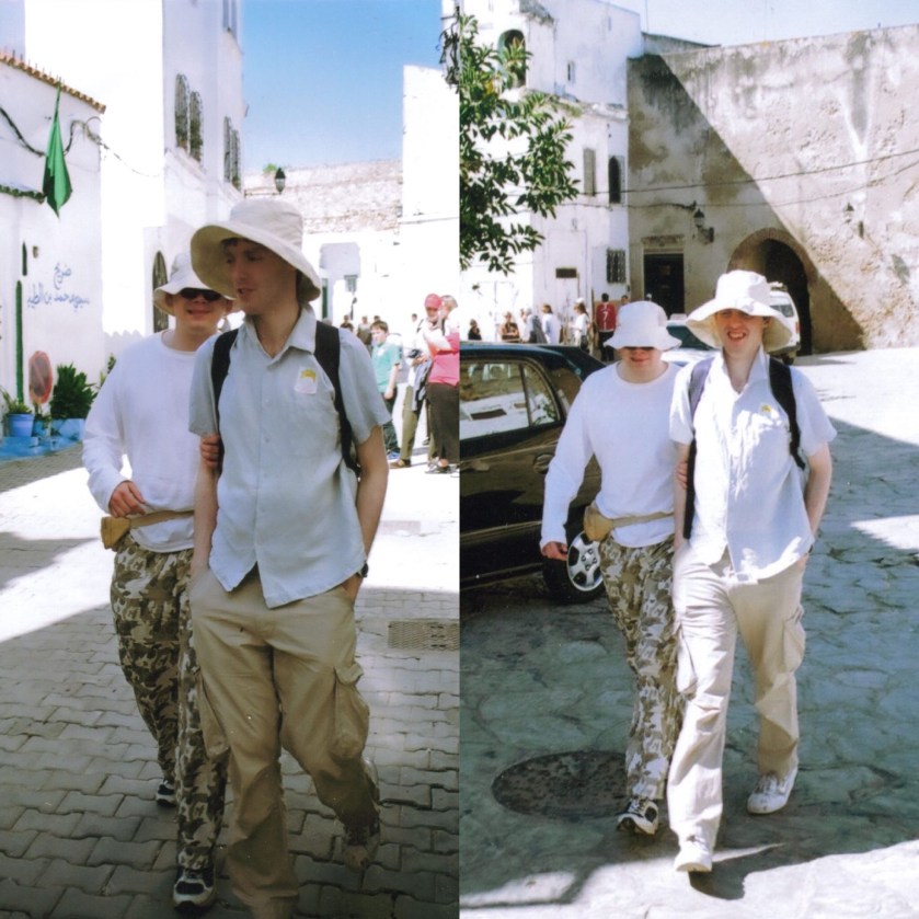 2 photos side by side of me and my male friend walking through the streets of Tangier, Morocco, in the bright sunshine, with tall white buildings in the background. We're wearing white sunhats and white tops. I'm wearing cream cargo trousers, while my friend is wearing trousers with an army camouflage pattern.