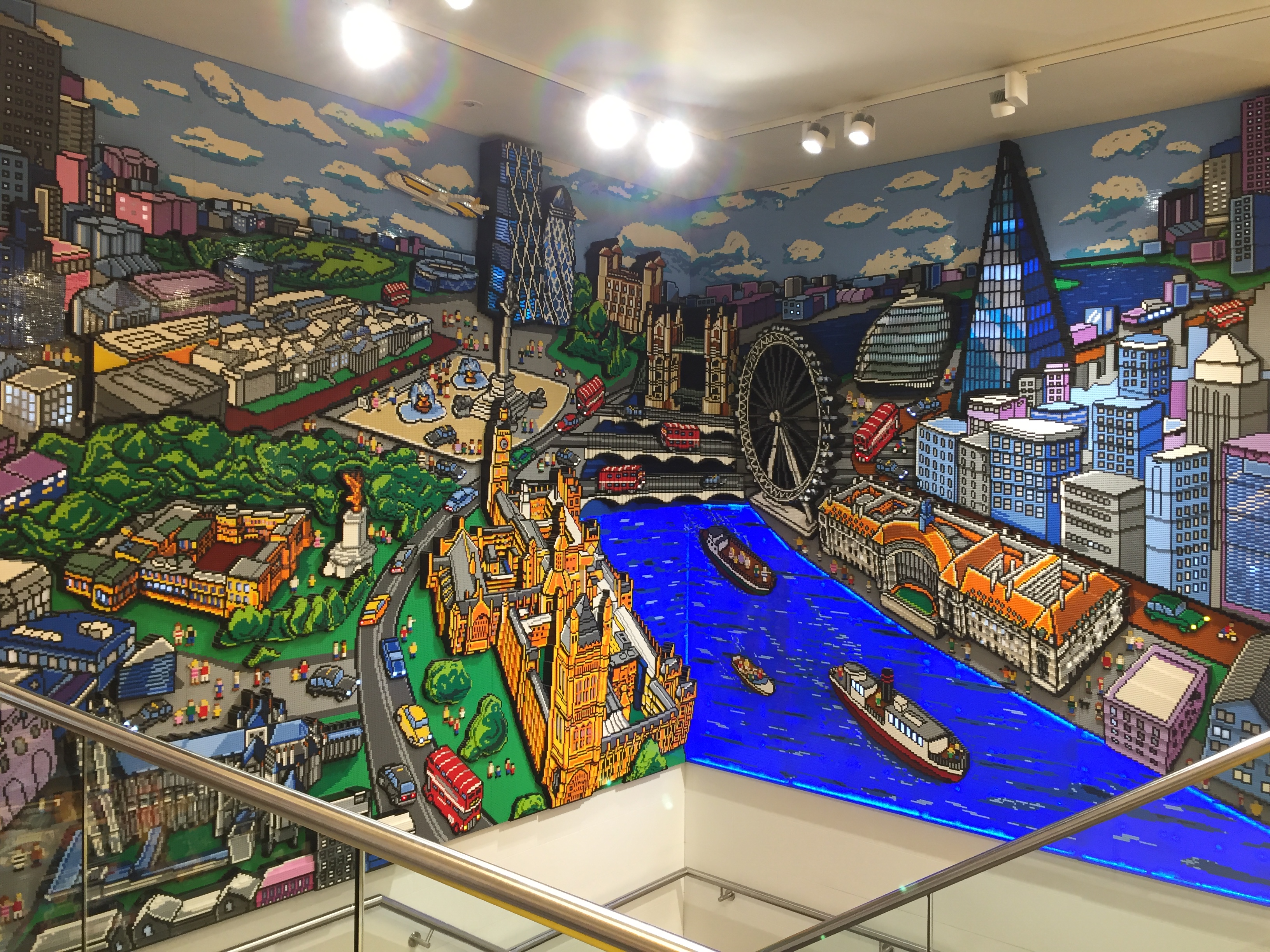 Large colourful Lego artwork of an aerial view of London, with the Thames in the centre, and iconic sights including Buckingham Palace, Trafalgar Square, Big Ben, The Houses of Parliament, Tower Bridge, The London Eye & The Shard.