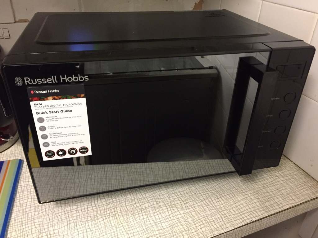 Russell Hobbs microwave, black in colour. The large door has a big window and a chunky handle on the right hand side to open it, and to the right of that is a small display for the time and 4 large round buttons positioned vertically below it.