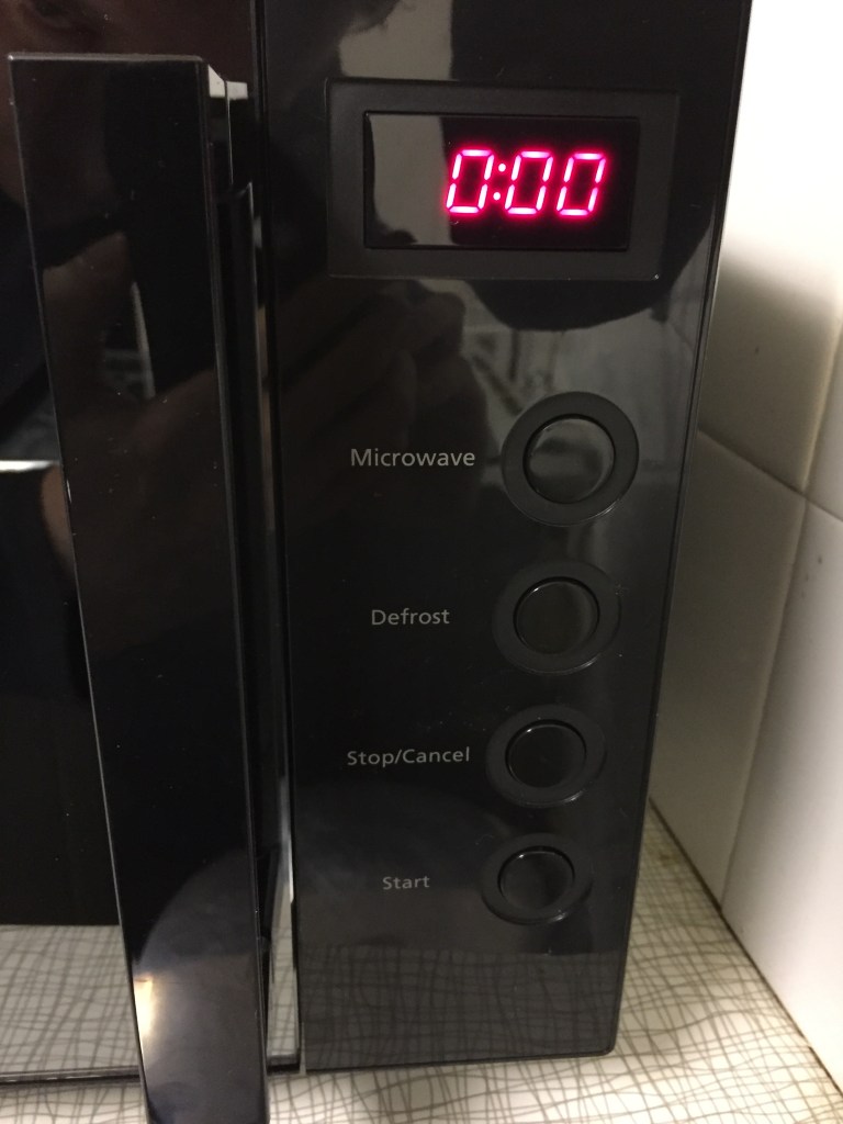 The right side of the black coloured microwave. A screen at the top shows the time in clear red figures. Below this are 4 large round buttons, each with white text to the left of them - for Microwave, Defrost, Stop and Start respectively.