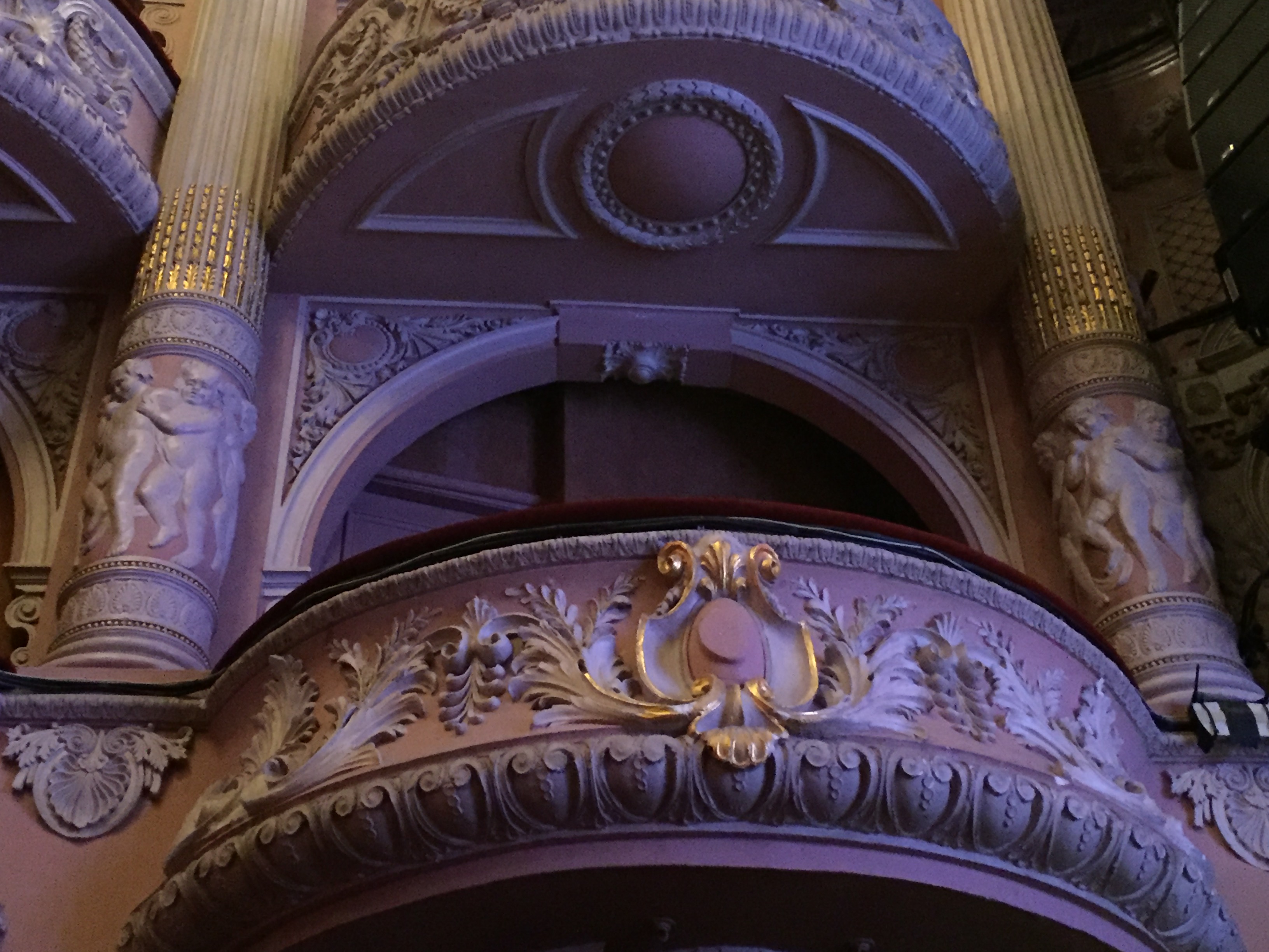 View from below of one of the curved balconies for the box seats in the auditorium, with ornate wing-like imagery embossed on the front of the balcony.